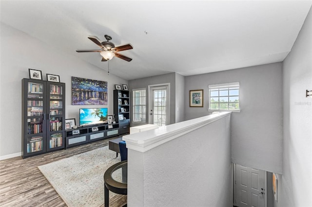 interior space with wood finished floors, baseboards, a ceiling fan, and vaulted ceiling