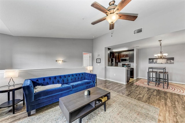 living area featuring visible vents, ceiling fan with notable chandelier, baseboards, and wood finished floors