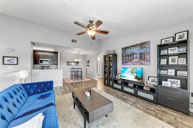living area featuring arched walkways, a ceiling fan, vaulted ceiling, visible vents, and wood finished floors
