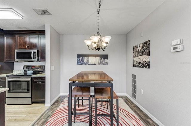 dining space with a chandelier, light wood-style floors, baseboards, and visible vents