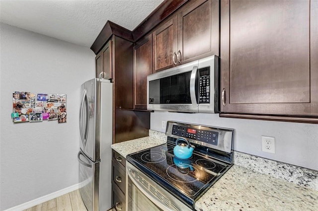kitchen featuring light stone counters, a textured ceiling, dark brown cabinets, appliances with stainless steel finishes, and light wood finished floors