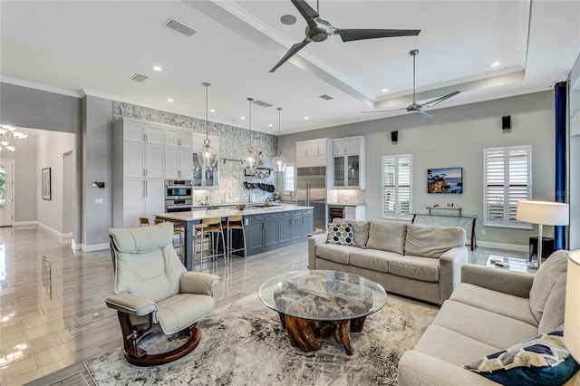 living room featuring ceiling fan with notable chandelier, ornamental molding, and a tray ceiling