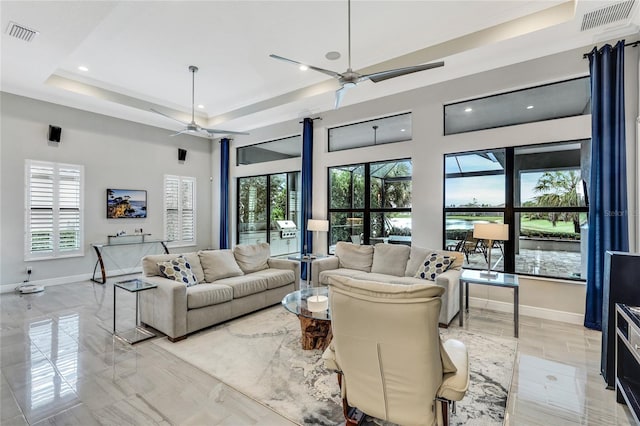 living room featuring ceiling fan, a tray ceiling, a high ceiling, and a wealth of natural light