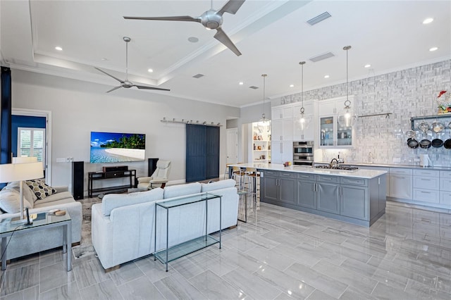 living room with ceiling fan, a tray ceiling, and ornamental molding