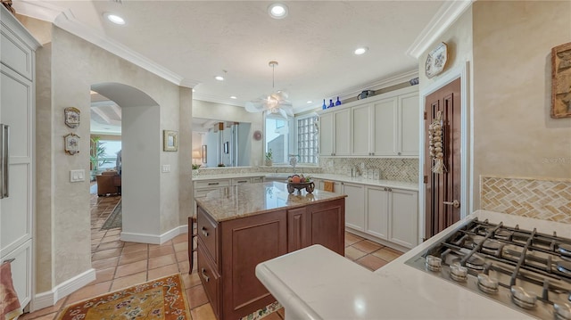 kitchen featuring crown molding, a wealth of natural light, white cabinets, and decorative light fixtures