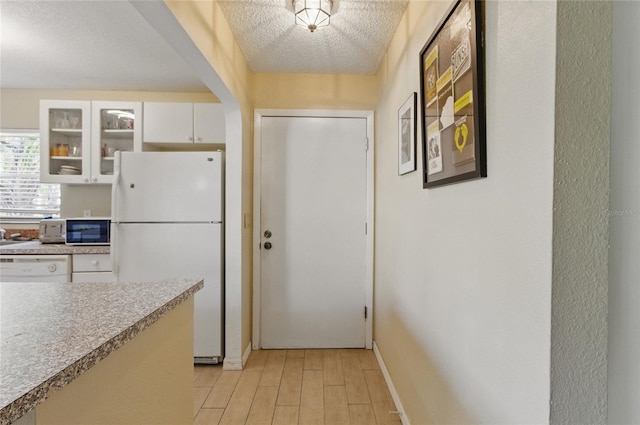 5071 Village Gardens Dr Unit 5, Sarasota, FL 34234 - kitchen with white appliances, glass insert cabinets, light countertops, white cabinets, and light wood-style floors