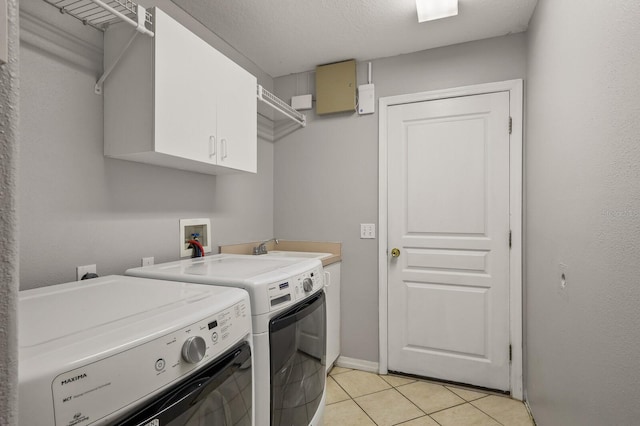 clothes washing area with washing machine and dryer, light tile patterned flooring, a textured ceiling, cabinets, and sink