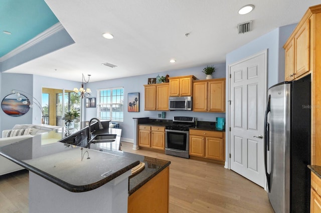 kitchen with appliances with stainless steel finishes, pendant lighting, light hardwood / wood-style flooring, a center island with sink, and a notable chandelier