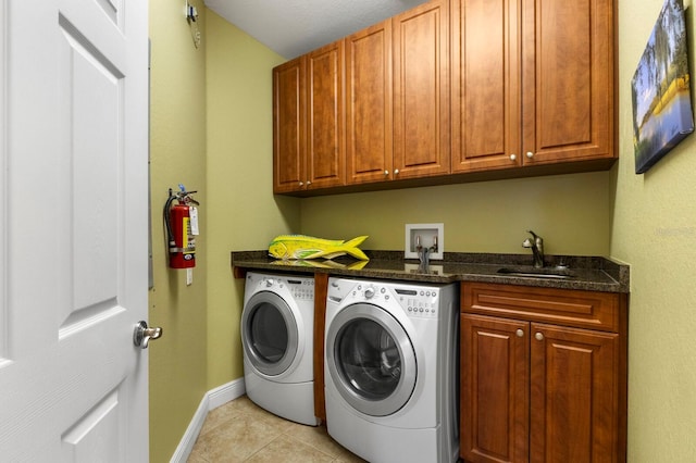 clothes washing area with cabinets, washing machine and dryer, light tile patterned floors, and sink