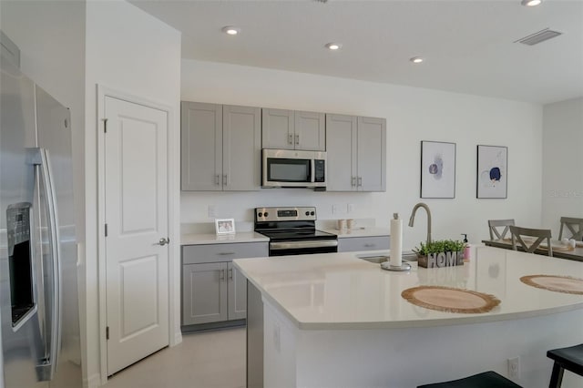 kitchen featuring gray cabinets, a kitchen island with sink, sink, a kitchen bar, and appliances with stainless steel finishes