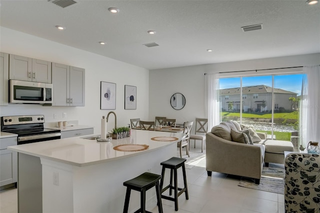 kitchen featuring appliances with stainless steel finishes, a kitchen breakfast bar, gray cabinets, a center island with sink, and sink