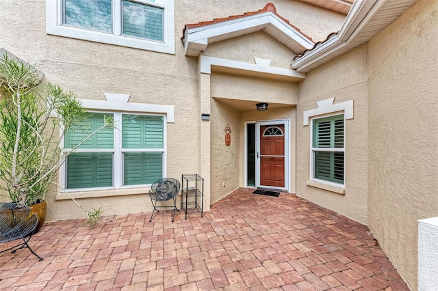 view of exterior entry with stucco siding and a patio area