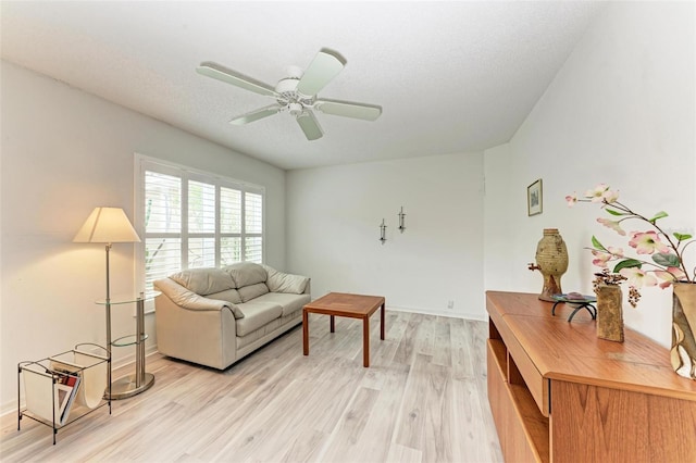 living room with ceiling fan, a textured ceiling, and light wood-type flooring