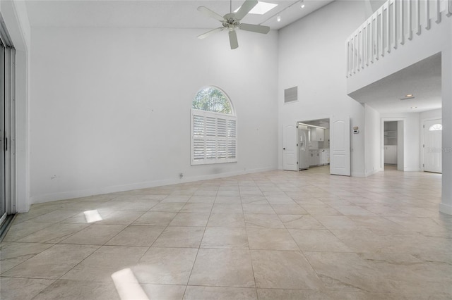 unfurnished living room featuring a ceiling fan, a towering ceiling, baseboards, and visible vents