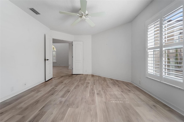empty room with light wood finished floors, baseboards, visible vents, and ceiling fan