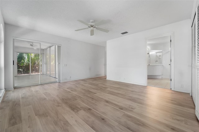 spare room with baseboards, a textured ceiling, light wood-style floors, visible vents, and ceiling fan