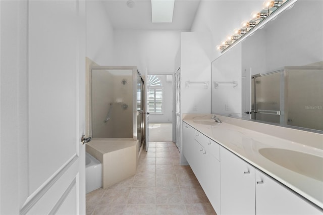 bathroom with tile patterned floors, a sink, a shower stall, a skylight, and double vanity
