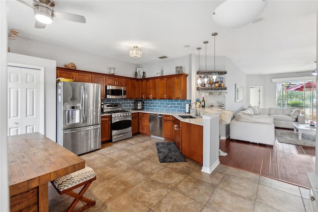 kitchen with hanging light fixtures, sink, tasteful backsplash, appliances with stainless steel finishes, and light wood-type flooring