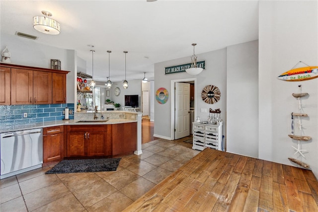 kitchen with hanging light fixtures, decorative backsplash, kitchen peninsula, stainless steel dishwasher, and sink