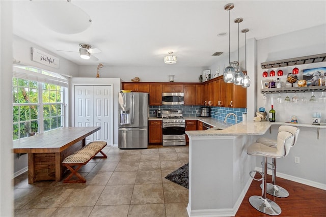 kitchen with kitchen peninsula, a kitchen bar, hanging light fixtures, stainless steel appliances, and backsplash