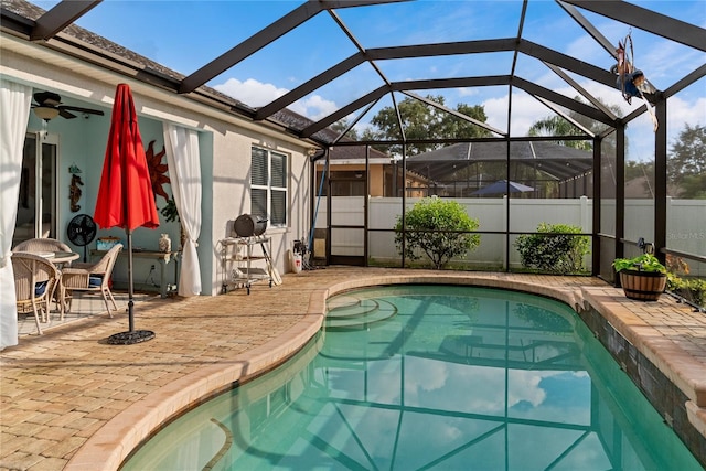 view of swimming pool with glass enclosure, ceiling fan, and a patio area