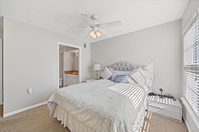 bedroom featuring ceiling fan, light colored carpet, and ensuite bath