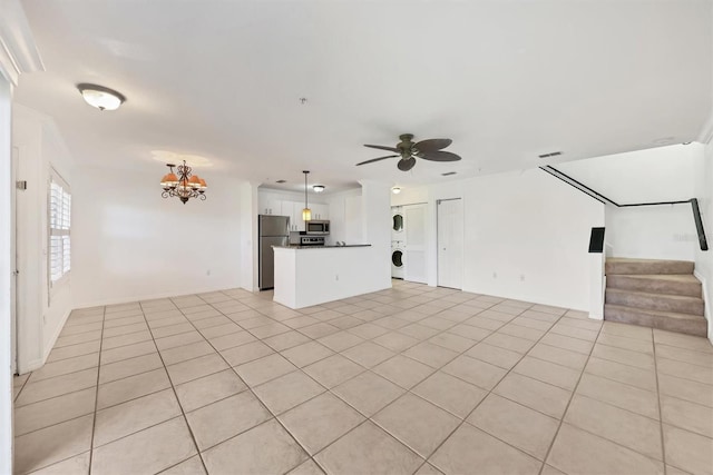 unfurnished living room with stacked washing maching and dryer, light tile patterned flooring, and ceiling fan