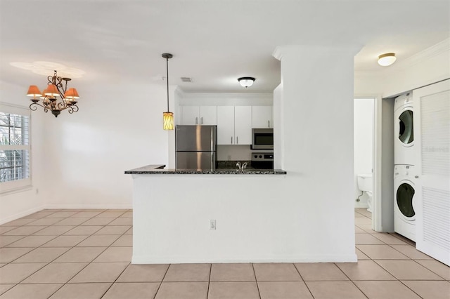 kitchen with hanging light fixtures, white cabinetry, stainless steel appliances, dark stone countertops, and stacked washing maching and dryer