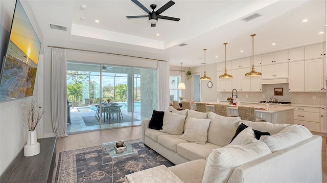 living room featuring wood-type flooring, a raised ceiling, and ceiling fan