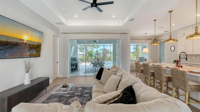 living room featuring ceiling fan, a raised ceiling, and light wood-type flooring