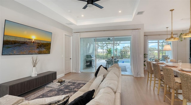 living room with a tray ceiling, light hardwood / wood-style floors, and ceiling fan