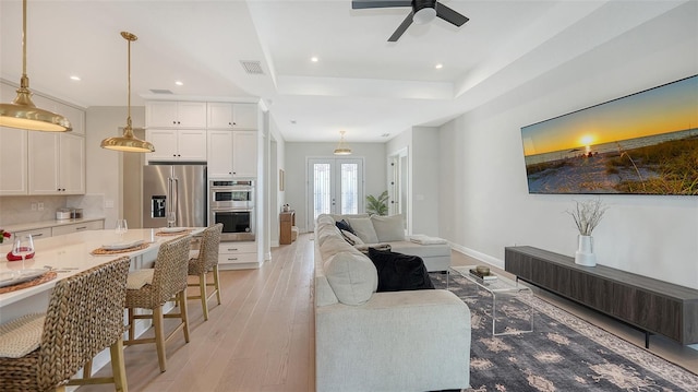 living room with light hardwood / wood-style floors, french doors, a tray ceiling, and ceiling fan