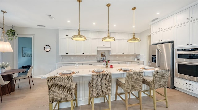 kitchen featuring a center island with sink, appliances with stainless steel finishes, white cabinetry, pendant lighting, and light hardwood / wood-style floors