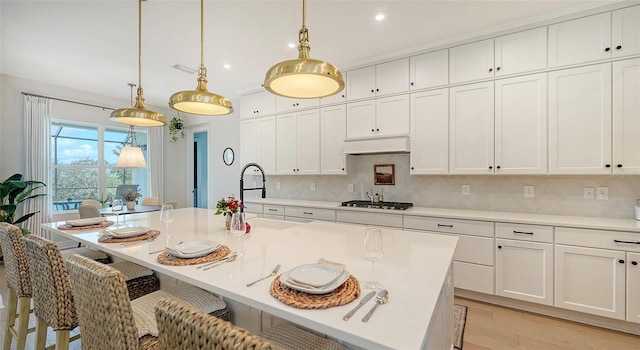 kitchen with custom exhaust hood, an island with sink, decorative light fixtures, and light wood-type flooring