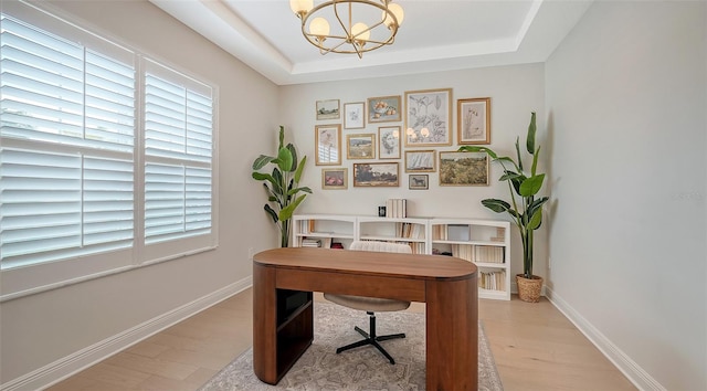 home office with light hardwood / wood-style floors, a notable chandelier, and a tray ceiling