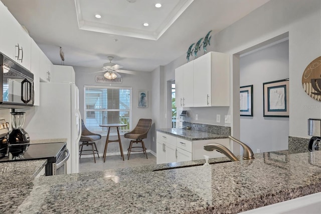 kitchen featuring white cabinets, kitchen peninsula, a tray ceiling, ceiling fan, and stainless steel range with electric cooktop