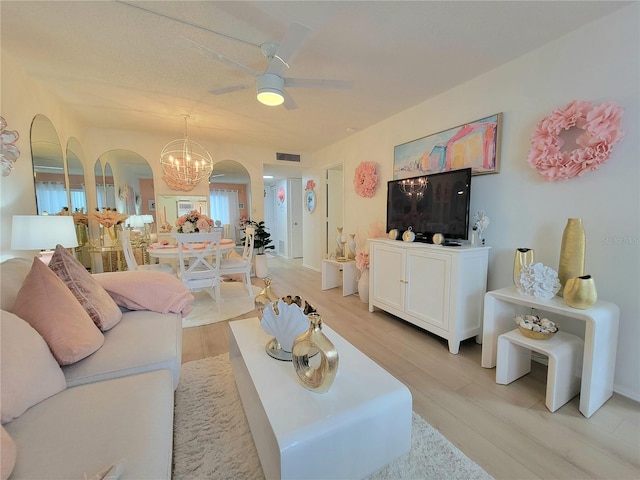 living room with ceiling fan with notable chandelier and light hardwood / wood-style floors