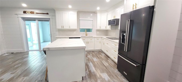 kitchen with light wood-type flooring, black appliances, a kitchen island, and white cabinetry