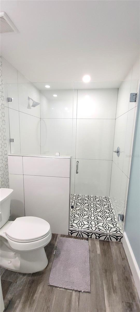 bathroom featuring walk in shower, hardwood / wood-style floors, and toilet