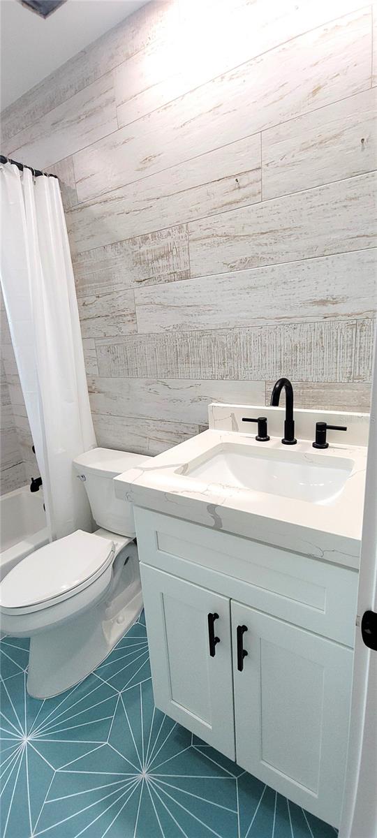 full bathroom with tile walls, vanity, tile patterned flooring, shower / tub combo with curtain, and toilet