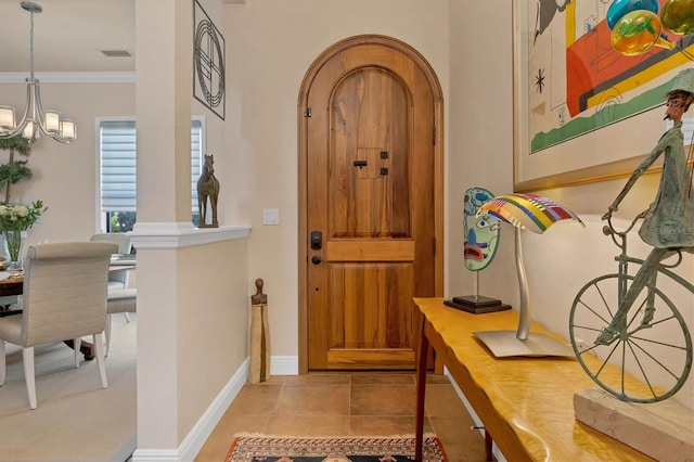 tiled foyer with ornamental molding and an inviting chandelier