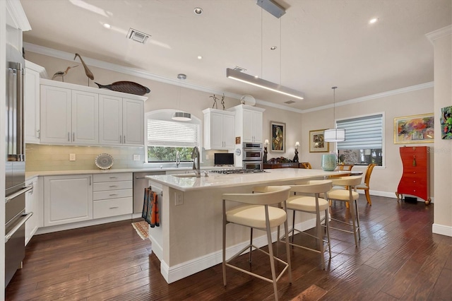 kitchen with white cabinets, a center island with sink, dark hardwood / wood-style flooring, appliances with stainless steel finishes, and pendant lighting