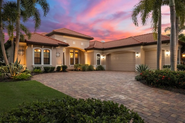 mediterranean / spanish home with stucco siding, an attached garage, a tile roof, and decorative driveway