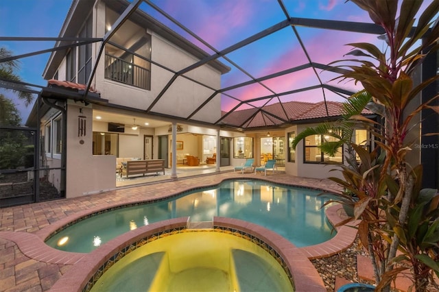 pool at dusk featuring a patio, glass enclosure, ceiling fan, and an in ground hot tub