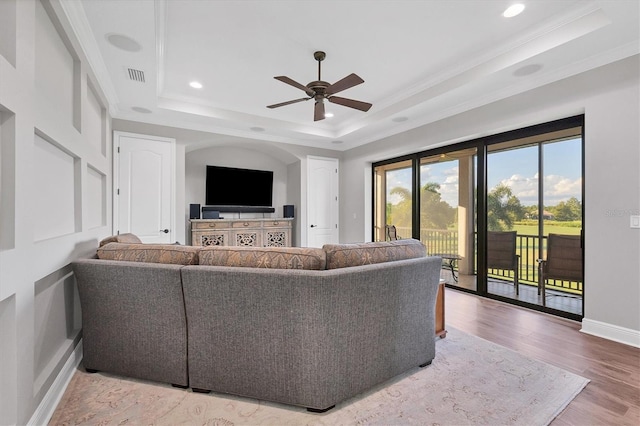 living room with ornamental molding, wood-type flooring, a tray ceiling, and ceiling fan