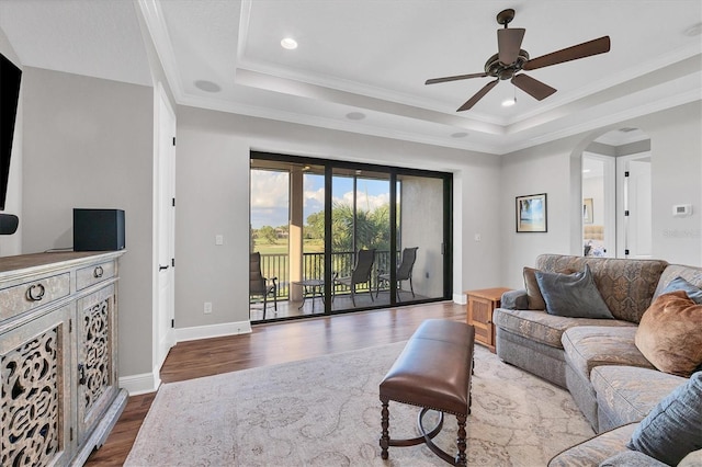 living room with ceiling fan, a tray ceiling, dark hardwood / wood-style floors, and crown molding