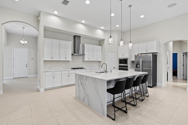 kitchen featuring wall chimney exhaust hood, a large island with sink, stainless steel appliances, and white cabinetry