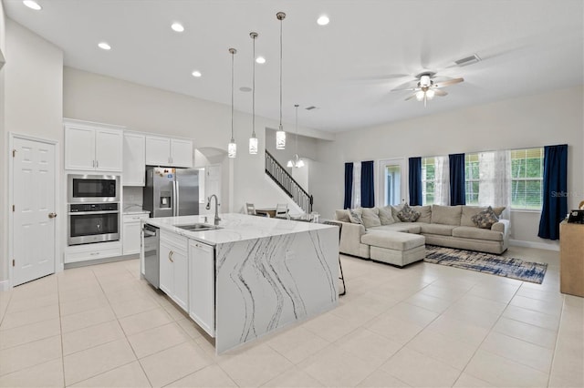 kitchen with light stone counters, sink, white cabinets, a center island with sink, and appliances with stainless steel finishes