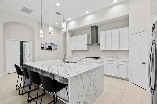 kitchen with wall chimney exhaust hood, a kitchen island with sink, sink, and white cabinetry