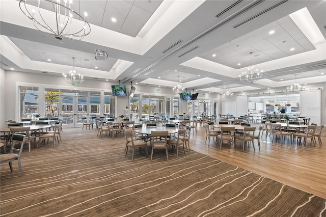 dining room featuring hardwood / wood-style flooring, french doors, a raised ceiling, an inviting chandelier, and a healthy amount of sunlight